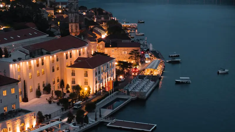 A coastal town in the Bay of Kotor at dusk — stone houses, a bell tower and boats in the bay