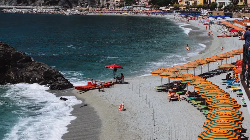 A Mediterranean beach with umbrellas, sunbeds and a rocky headland